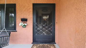 A black door with a metal security gate, a small wall-mounted light fixture, and a hanging chain.