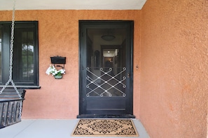 A black door with a metal security gate, a small wall-mounted light fixture, and a hanging chain.