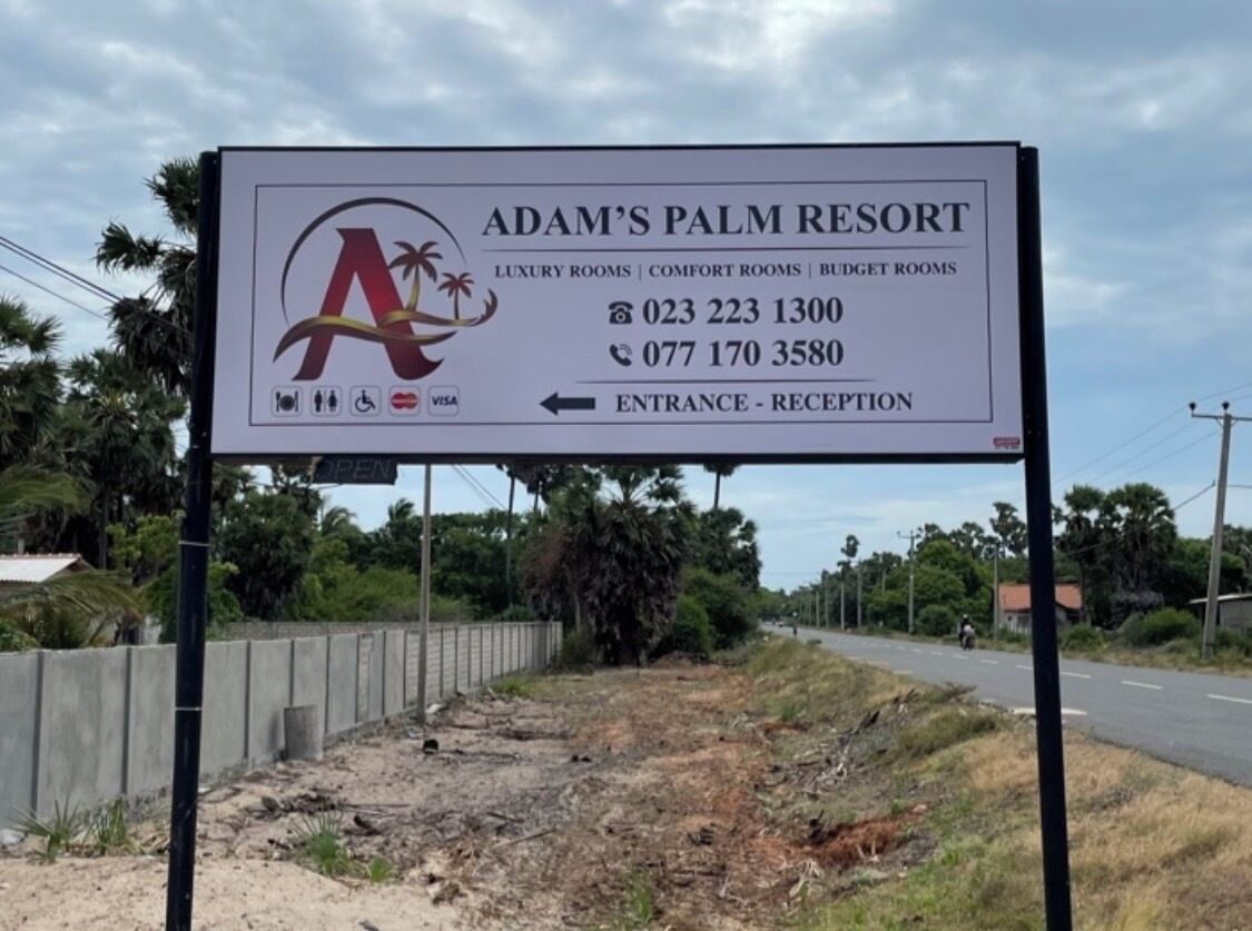 A sign for Adam's Palm Resort with contact numbers and a directional arrow to the entrance.