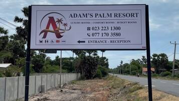 A sign for Adam's Palm Resort with contact numbers and a directional arrow to the entrance.