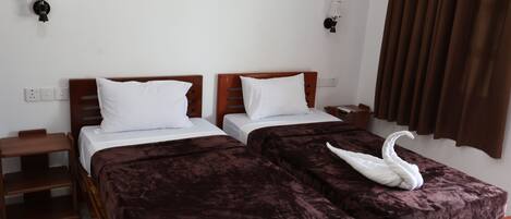 A hotel room with two beds, each with a wooden headboard, white bedding, and a brown velvet bedspread. There are two bedside tables with lamps, a brown curtain, and a wall socket.