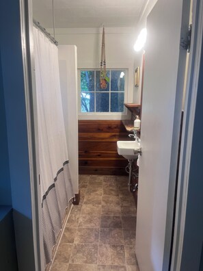 A narrow bathroom with a window, a wooden panel wall, a sink, and a shower curtain.