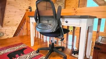 Een houten blokhut inrichting met een bureau, stoel en een kleed met een patroon.