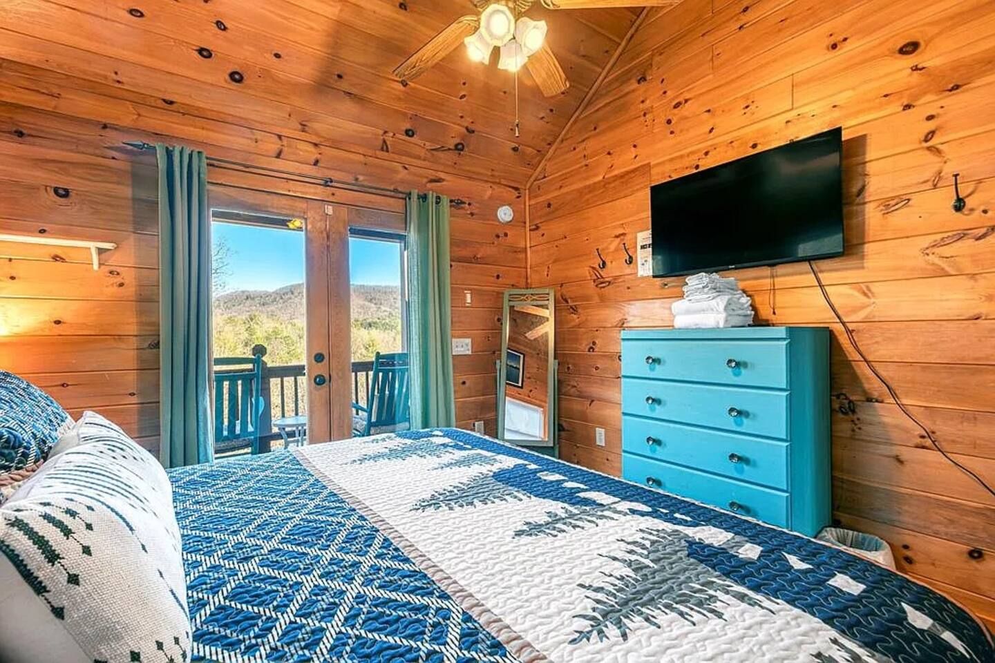 Een houten slaapkamer met een bed, een dressoir, een televisie en een balkon met uitzicht.