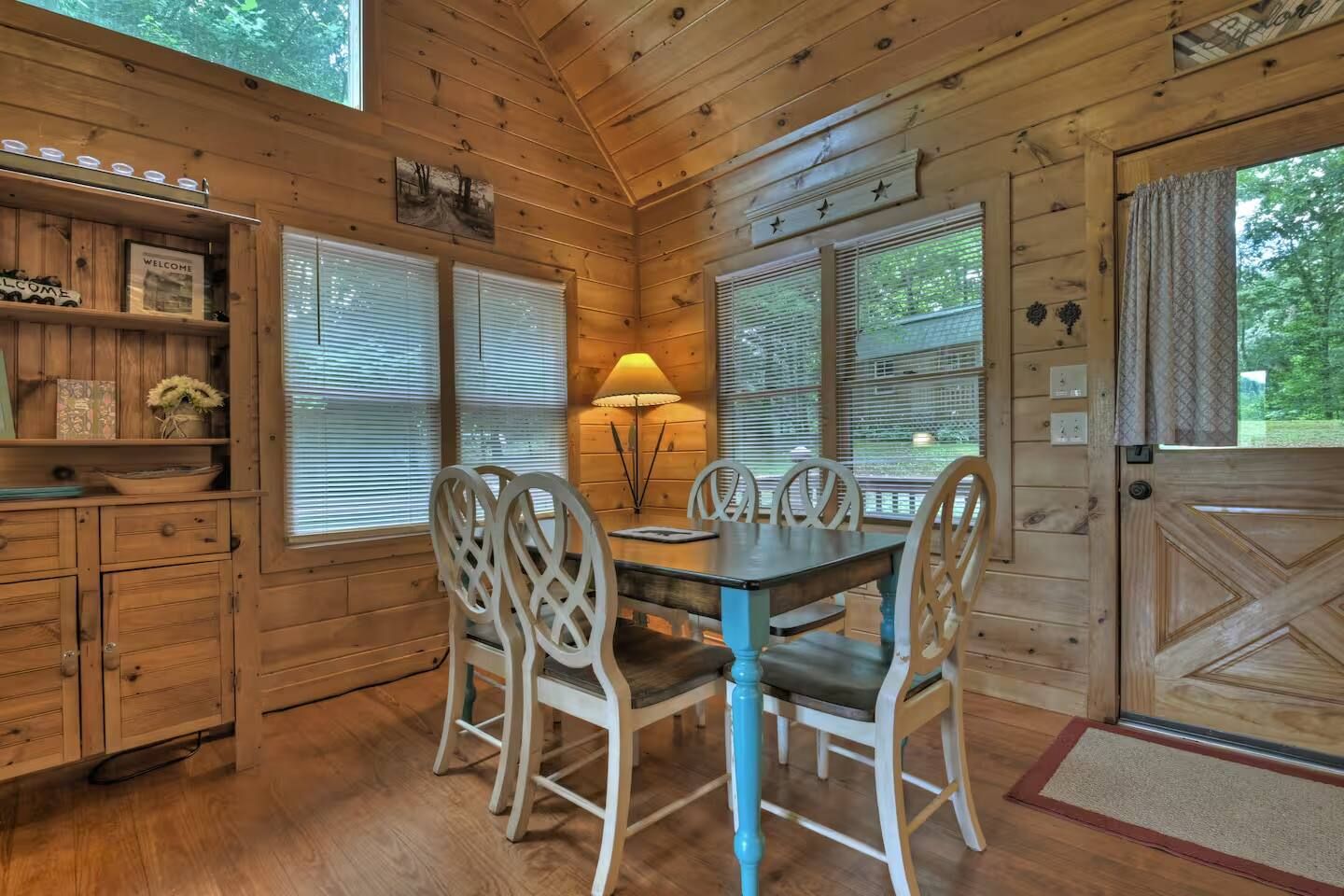 L’intérieur d’un chalet en bois, avec une table et des chaises, une lampe et une porte ornée d’un panneau décoratif.