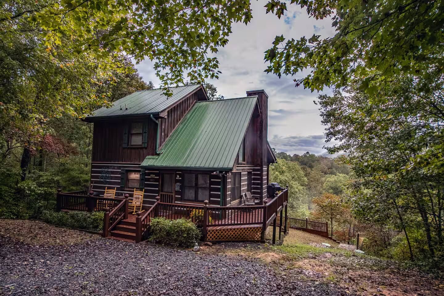 A rustic log cabin with a metal roof, surrounded by dense forest.