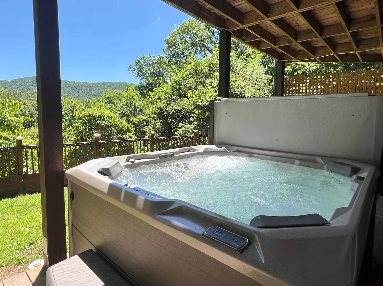 A hot tub with a control panel, set on a wooden deck with a view of greenery and hills.