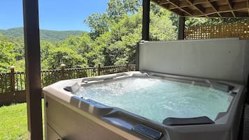A hot tub with a control panel, set on a wooden deck with a view of greenery and hills.
