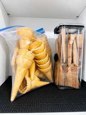 Ein Lagerbereich mit klaren Plastiktüten, die Eiswaffeln enthalten, und einem klaren Plastikbehälter mit Papiertüten, möglicherweise mit Keksen oder Snacks.