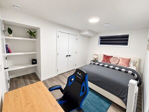 Ein Schlafzimmer mit einem Bett, einem Schreibtisch, einem Stuhl, einem Kleiderschrank und einem Fenster.