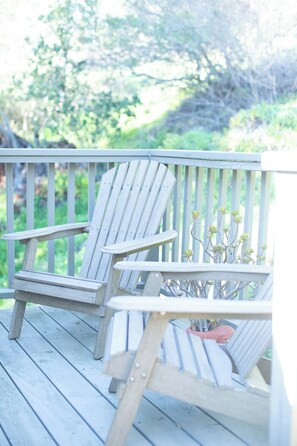 Two Adirondack chairs on a wooden deck with a railing, surrounded by greenery. - The Collected Cottage (Cambria)