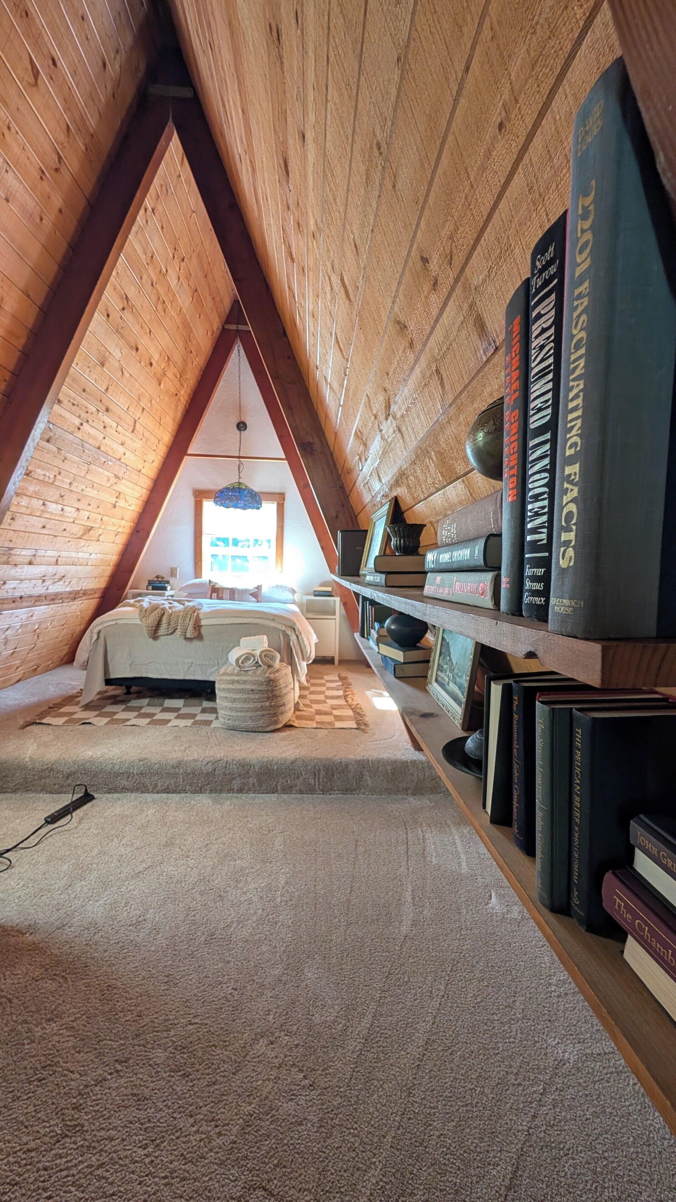 A cozy attic bedroom with a sloped ceiling, a bed, a bookshelf, and a window.