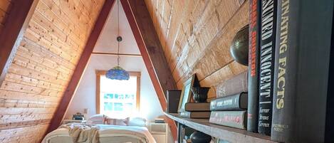 A cozy attic bedroom with a sloped ceiling, a bed, a bookshelf, and a window.