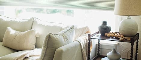 A cozy living room with a sofa, a side table with a lamp, and a window with blinds.