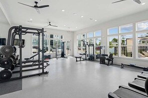 Ein geräumiges Fitnessstudio mit unterschiedlichen Trainingsgeräten, großen Fenstern und Deckenventilatoren.