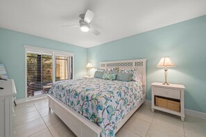 Quarto com cama, duas mesas de cabeceira com abajures, ventilador de teto e janela com persianas.