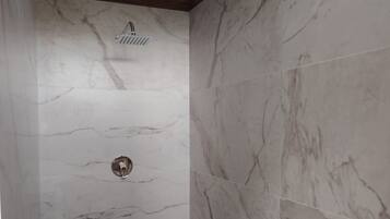A bathroom with marble walls, a shower, and a toilet.