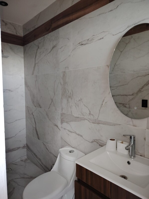 A bathroom with a marble wall, a toilet, a sink with a mirror, and a wooden vanity.