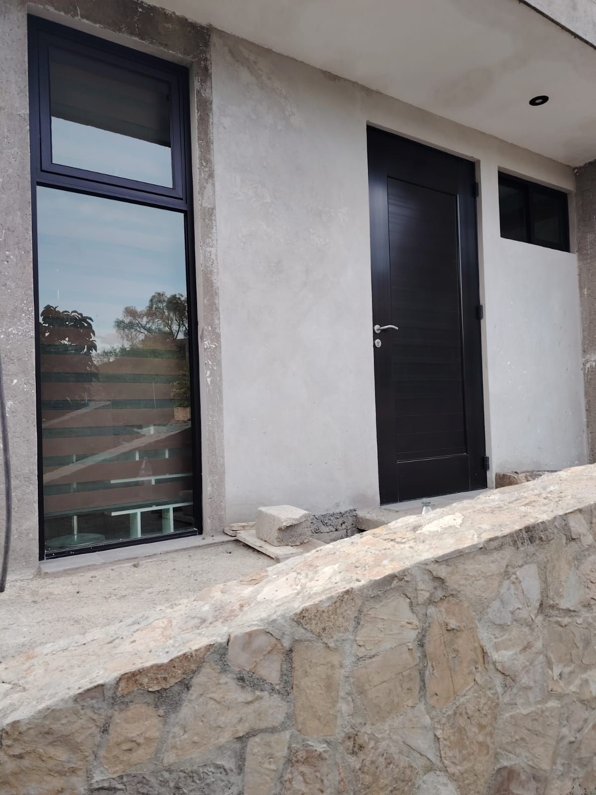 A building exterior with a stone retaining wall, a large window, and a black door.