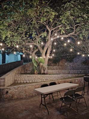 An outdoor dining area with a table and chairs, surrounded by a stone wall and a tree.
