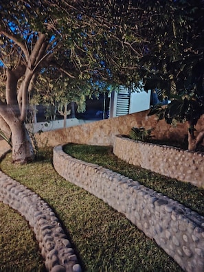 A landscaped garden with a curved stone pathway, a tree, and a low wall.