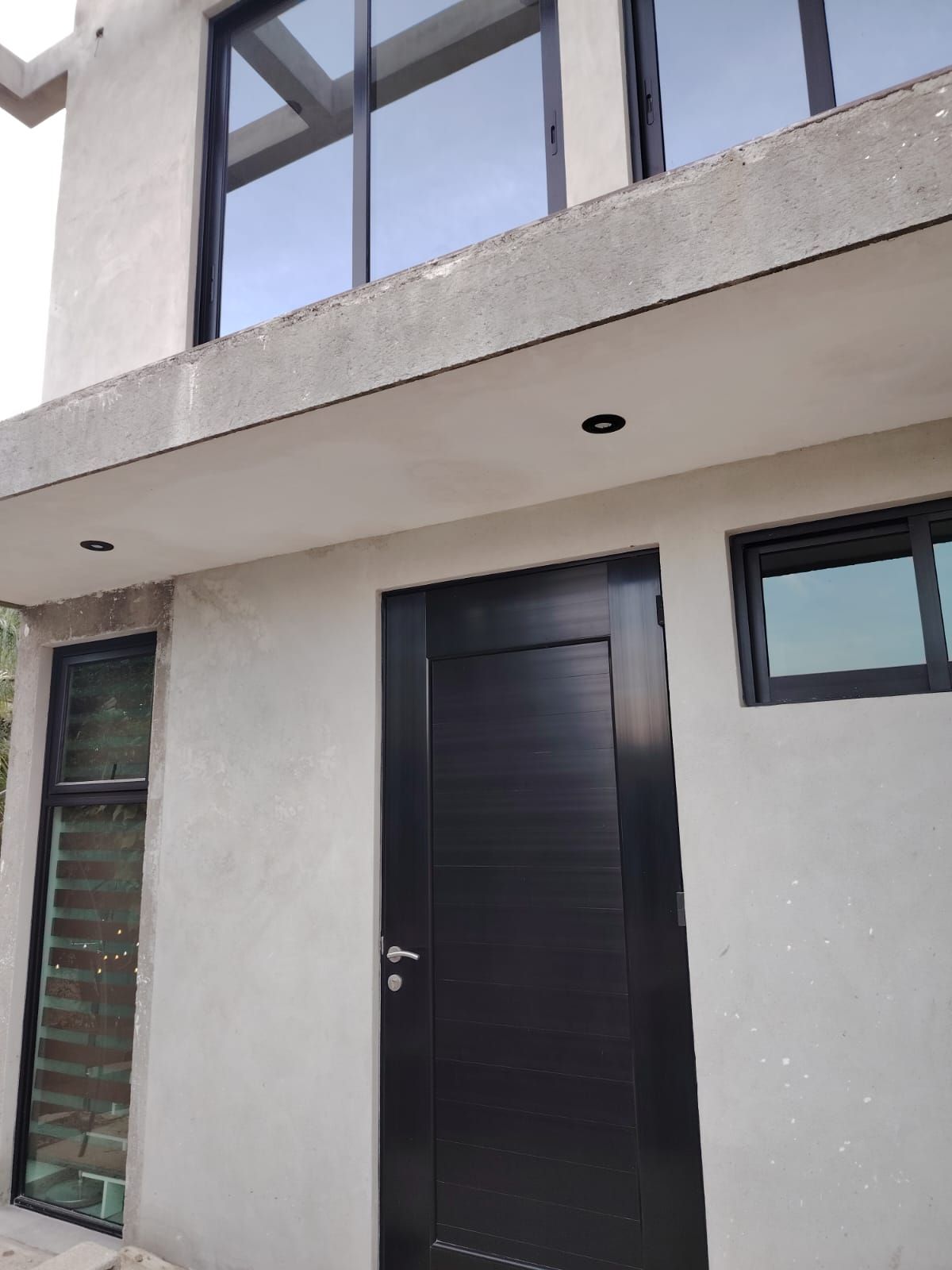 A modern building with a concrete facade, large windows, and a prominent black door.