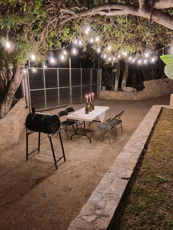 An outdoor patio with a barbecue grill, table, chairs, and string lights.