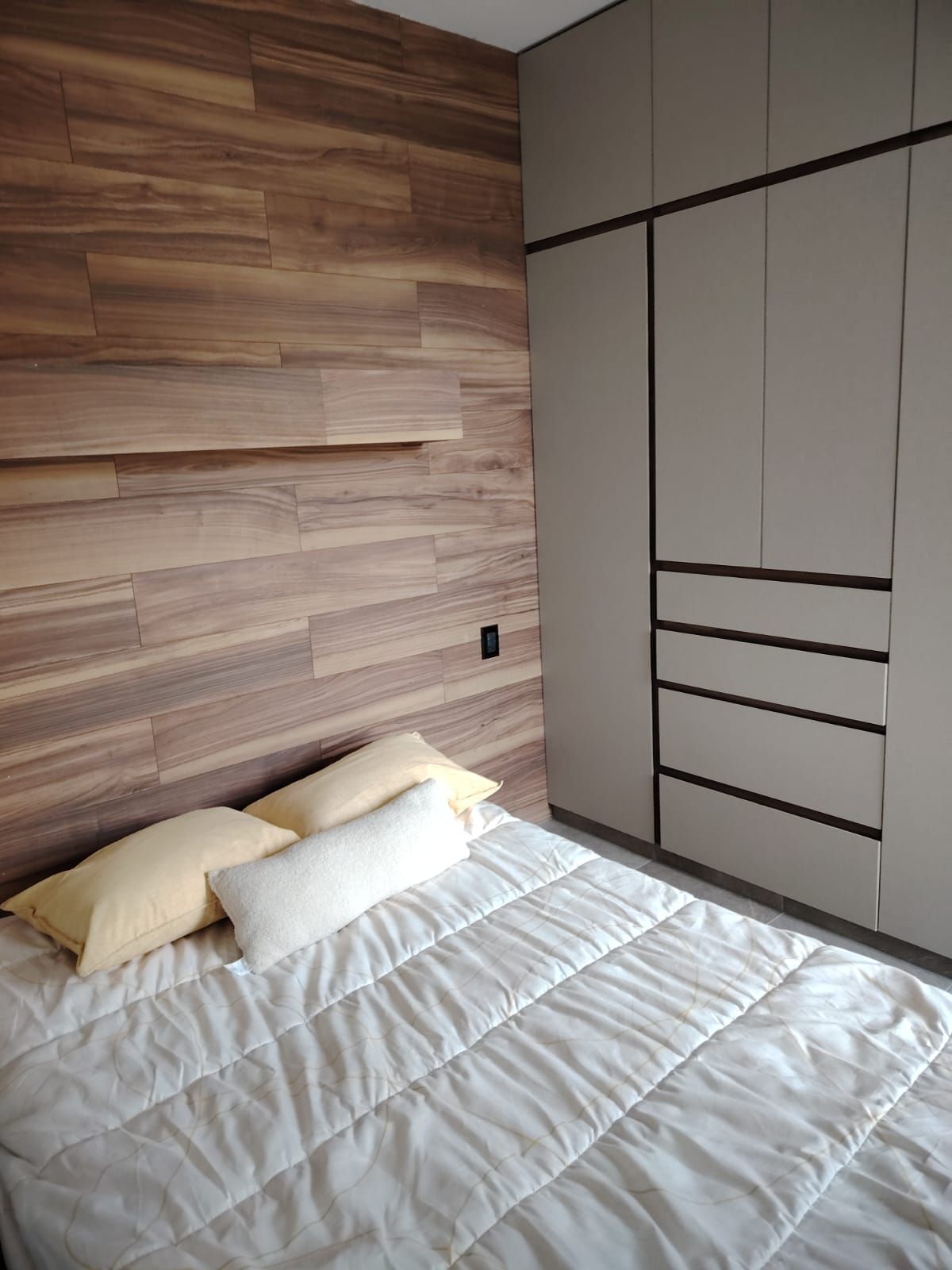 Ein Schlafzimmer mit einem hölzernen Kopfteil, einem Bett mit weißer Bettwäsche und einem Kleiderschrank mit vielen Fächern.