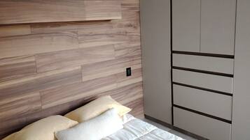 Ein Schlafzimmer mit einem hölzernen Kopfteil, einem Bett mit weißer Bettwäsche und einem Kleiderschrank mit vielen Fächern.