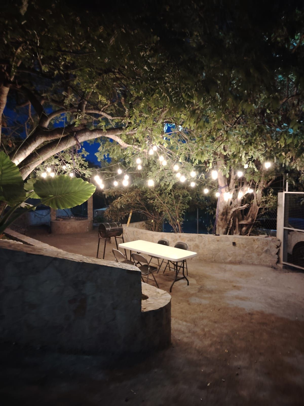 Eine Außenpatio-Terrasse mit Tisch und Stühlen, umgeben von Bäumen und Lichterketten.