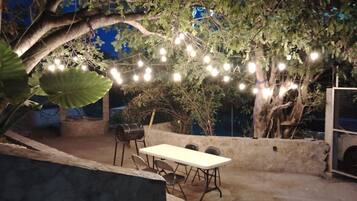 Eine Außenpatio-Terrasse mit Tisch und Stühlen, umgeben von Bäumen und Lichterketten.