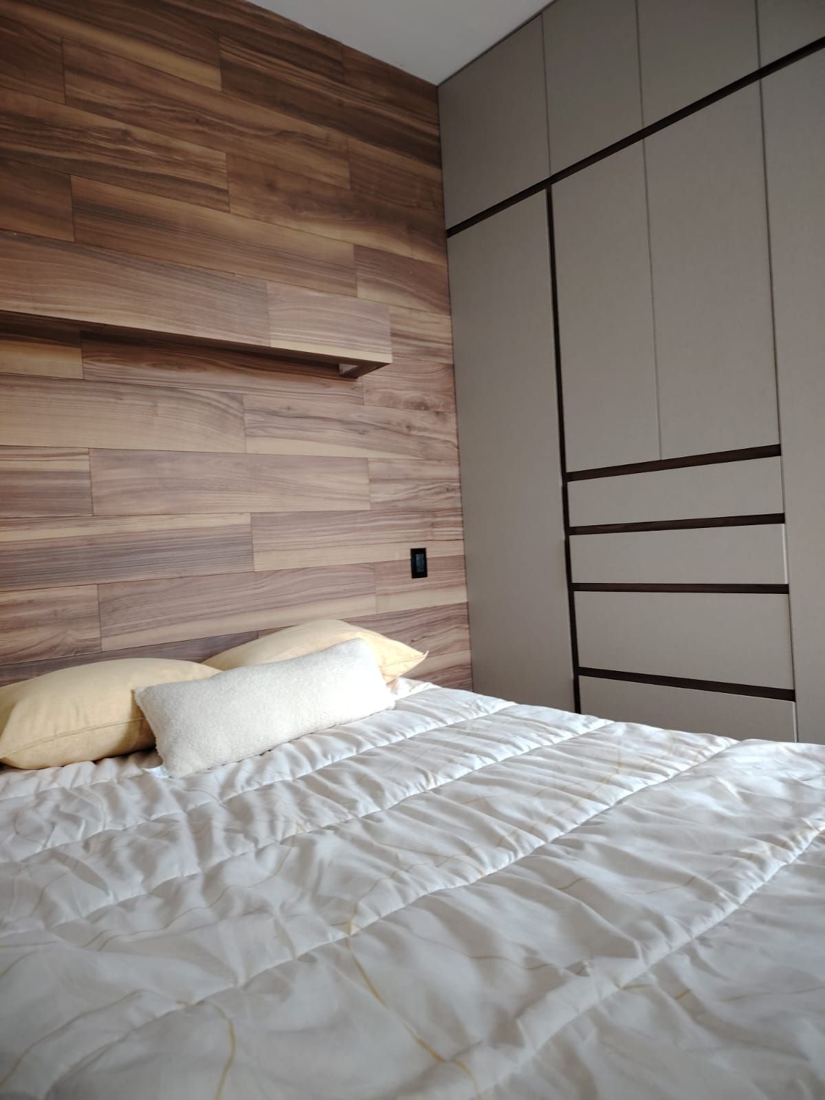 Une chambre à coucher avec un lit, des oreillers, une tête de lit en bois et une armoire.
