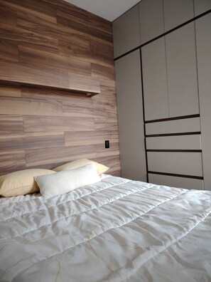 A bedroom with a bed, pillows, a wooden headboard, and a wardrobe.