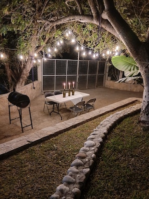 An outdoor patio area with a table and chairs, string lights, and a grill.
