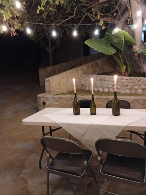 An outdoor dining area with a table and chairs, three lit candles, and string lights.