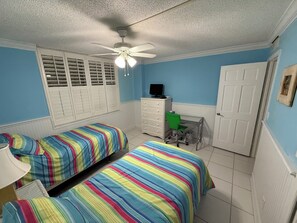 Ein Schlafzimmer mit zwei Betten, einem Schreibtisch, einem Stuhl, einem Fernseher und einer Tür.