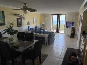 A living room with a glass dining table, dark patterned chairs, a ceiling fan, and a view of the ocean through a sliding glass door. - DIRECT OCEANFRONT • HUTCHINSON ISLAND • 2BR/2BA • WINTER SEASON (Jensen Beach)