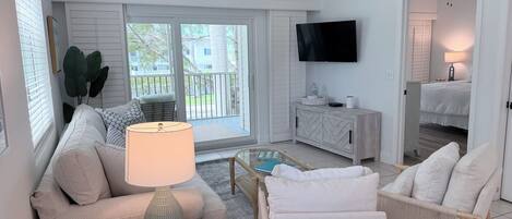 Un salon moderne avec un canapé, des fauteuils, une table basse, un téléviseur et un balcon offrant une vue agréable.