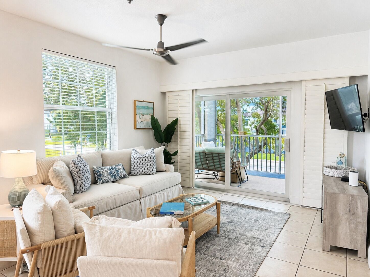 A living room with a sofa, armchairs, a coffee table, and a TV. There is a balcony with a chair and a table.