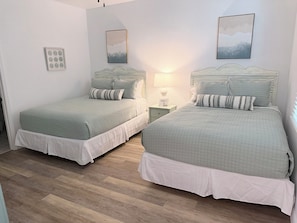 Ein Schlafzimmer mit zwei Betten, einem Nachttisch mit Lampe und gerahmten Kunstwerken an den Wänden.