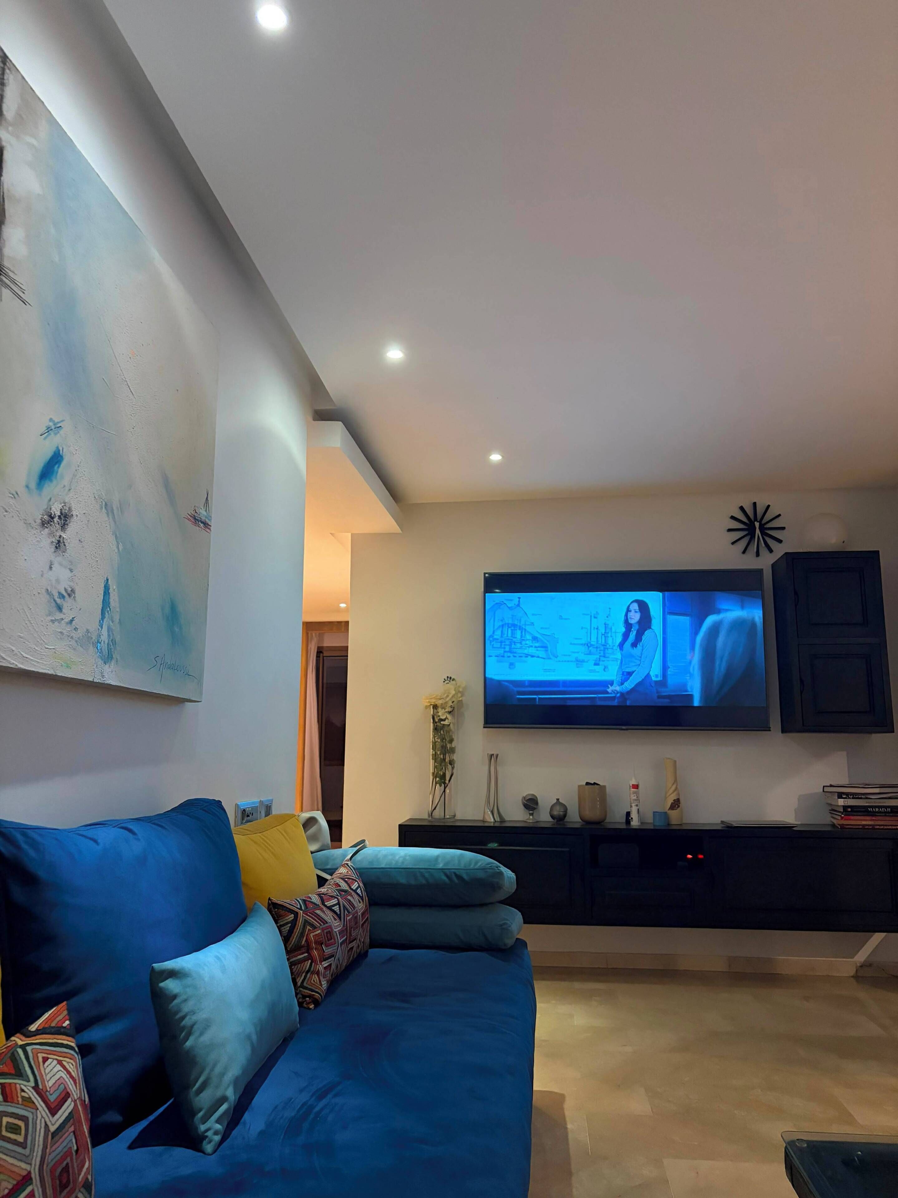 Ein modernes Wohnzimmer mit einem blauen Sofa, einem flachbildfernseher an der Wand und einem dekorativen Gegenstand darüber.
