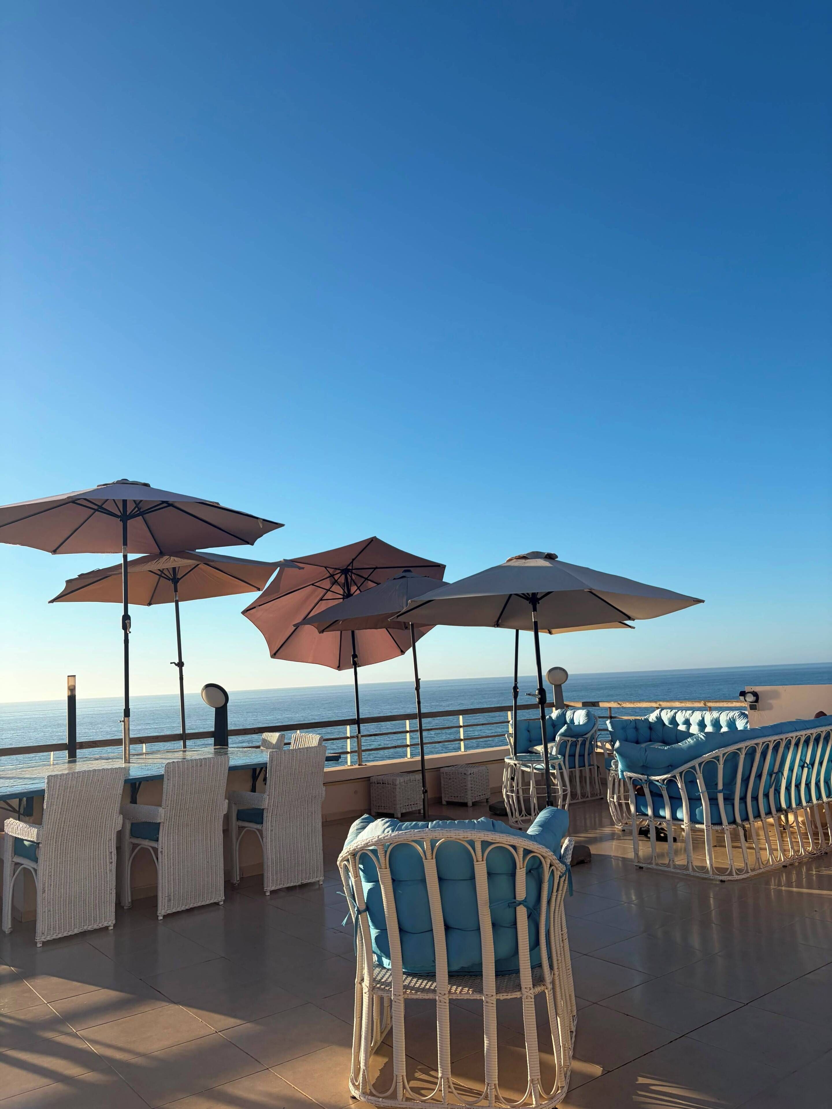 A terrace with wicker furniture, umbrellas, and a view of the sea.