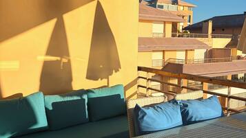A balcony with a wicker sofa and a glass-top table, overlooking a residential area.