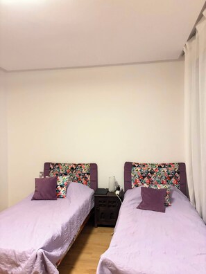 Ein Zimmer mit zwei Betten, jeweils mit einem blumigen Kopfteil und violetter Bettwäsche.