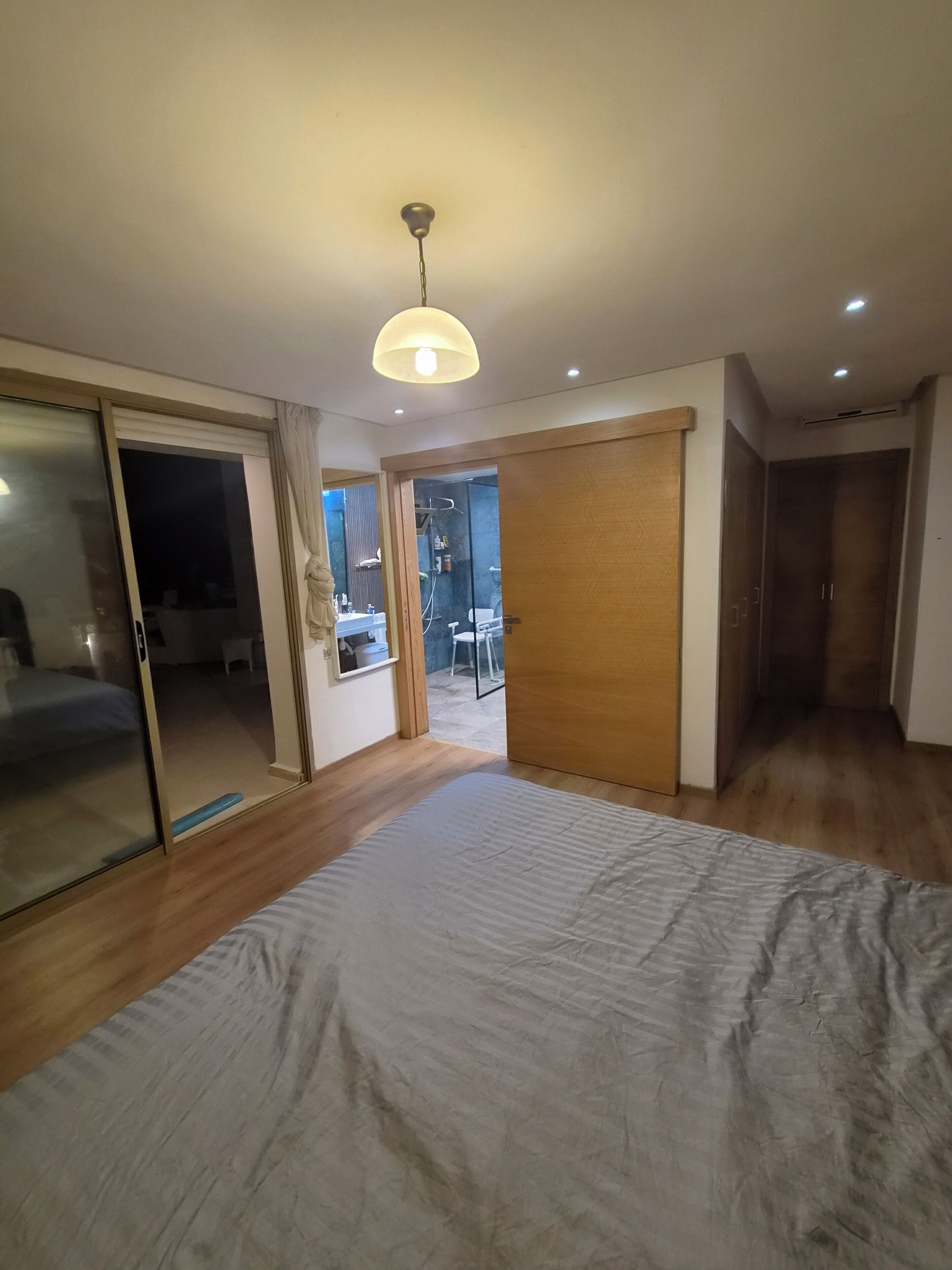 Une chambre avec un grand lit, une porte coulissante donnant sur un balcon et un luminaire au plafond.