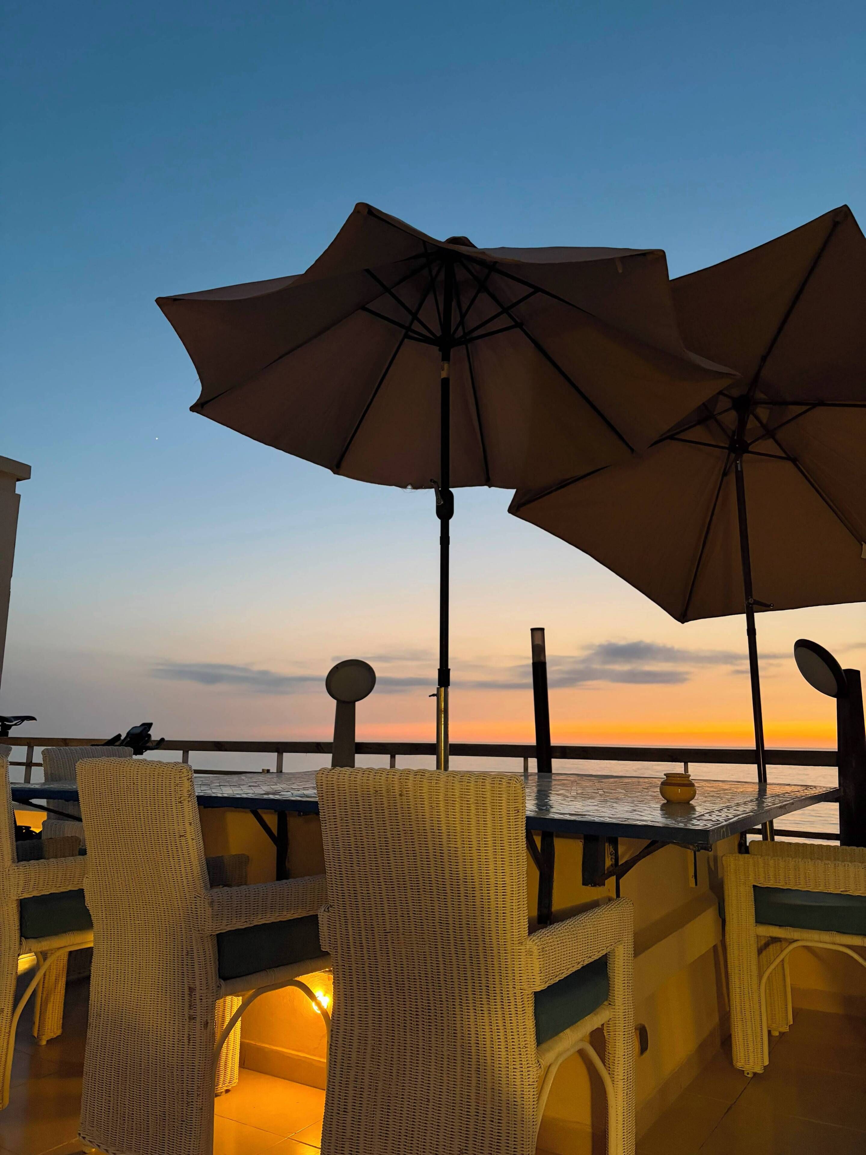 A terrace with wicker furniture, a table, and two large umbrellas.