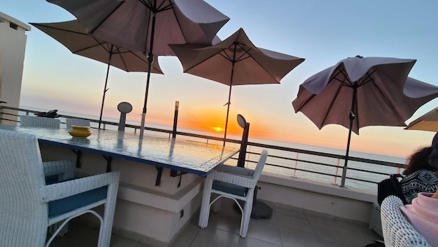 A terrace with a table and chairs, umbrellas, and a view of the sunset over the sea. - Best Sea View in Morocco, Wheelchair Friendly, Plage des Nations, Rabat, Kénitra (Plage des Nations)