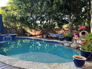 Ein Pool mit einer Steinterrasse, umgeben von Blumentöpfen und einer Hängematte.