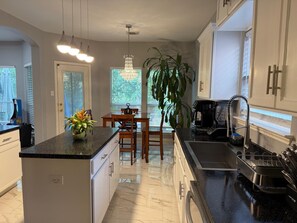 A modern kitchen with white cabinetry, a granite countertop, a dining area with a table and chairs, and a large window with a view of greenery. - Little oasis in Uptown San Antonio pool & jacuzzi (San Antonio)