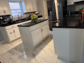 Een moderne keuken met witte kastjes, een roestvrijstalen koelkast en een marmeren vloer.